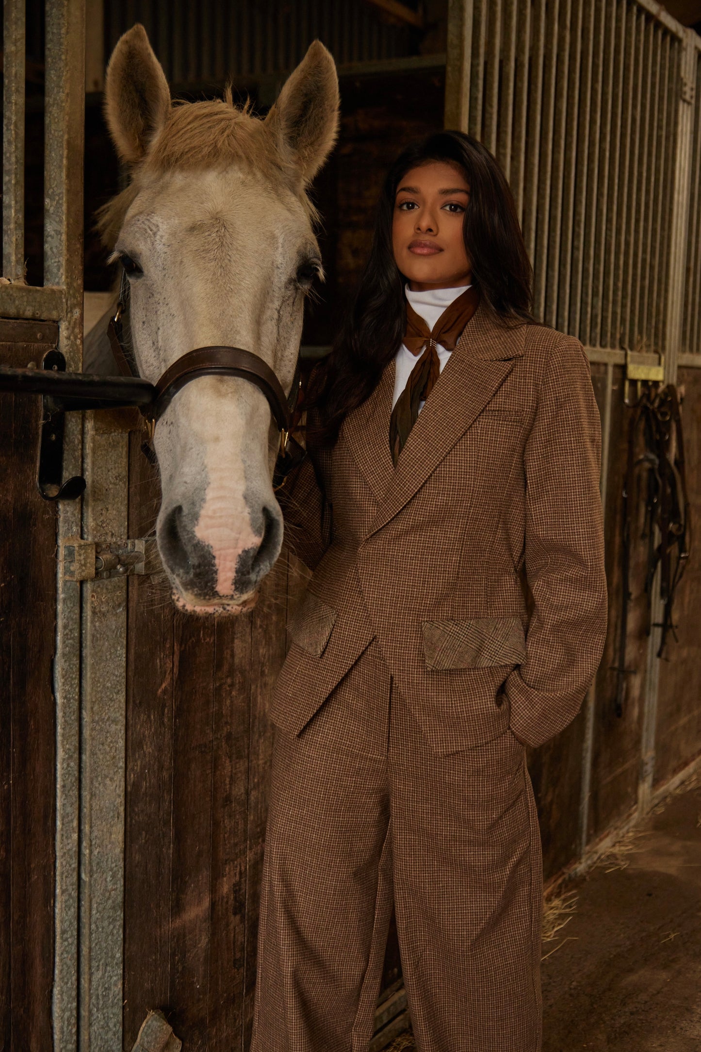 Woman in a brown suit standing next to a horse in a stable