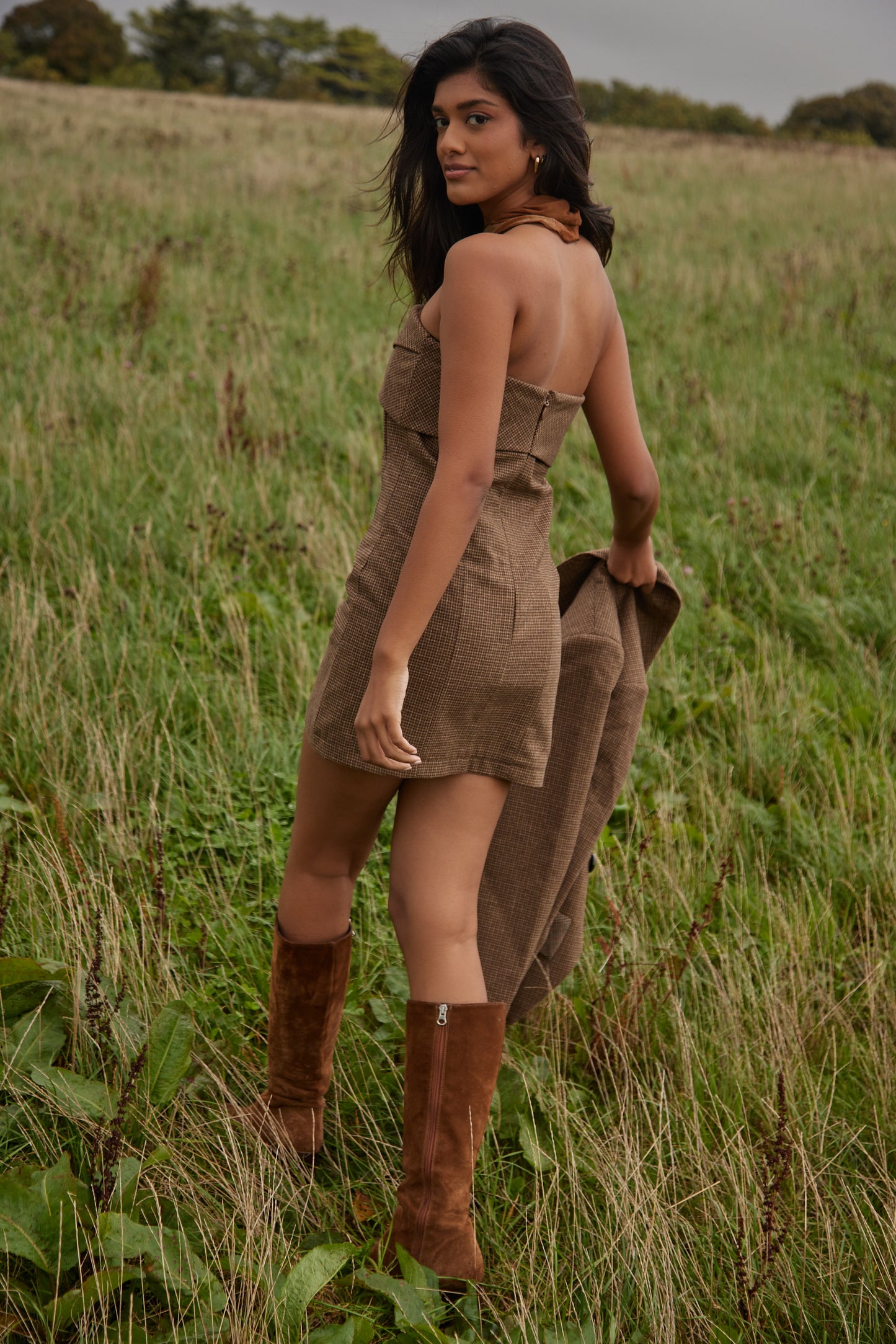 Woman in a brown dress and boots standing in a grassy field