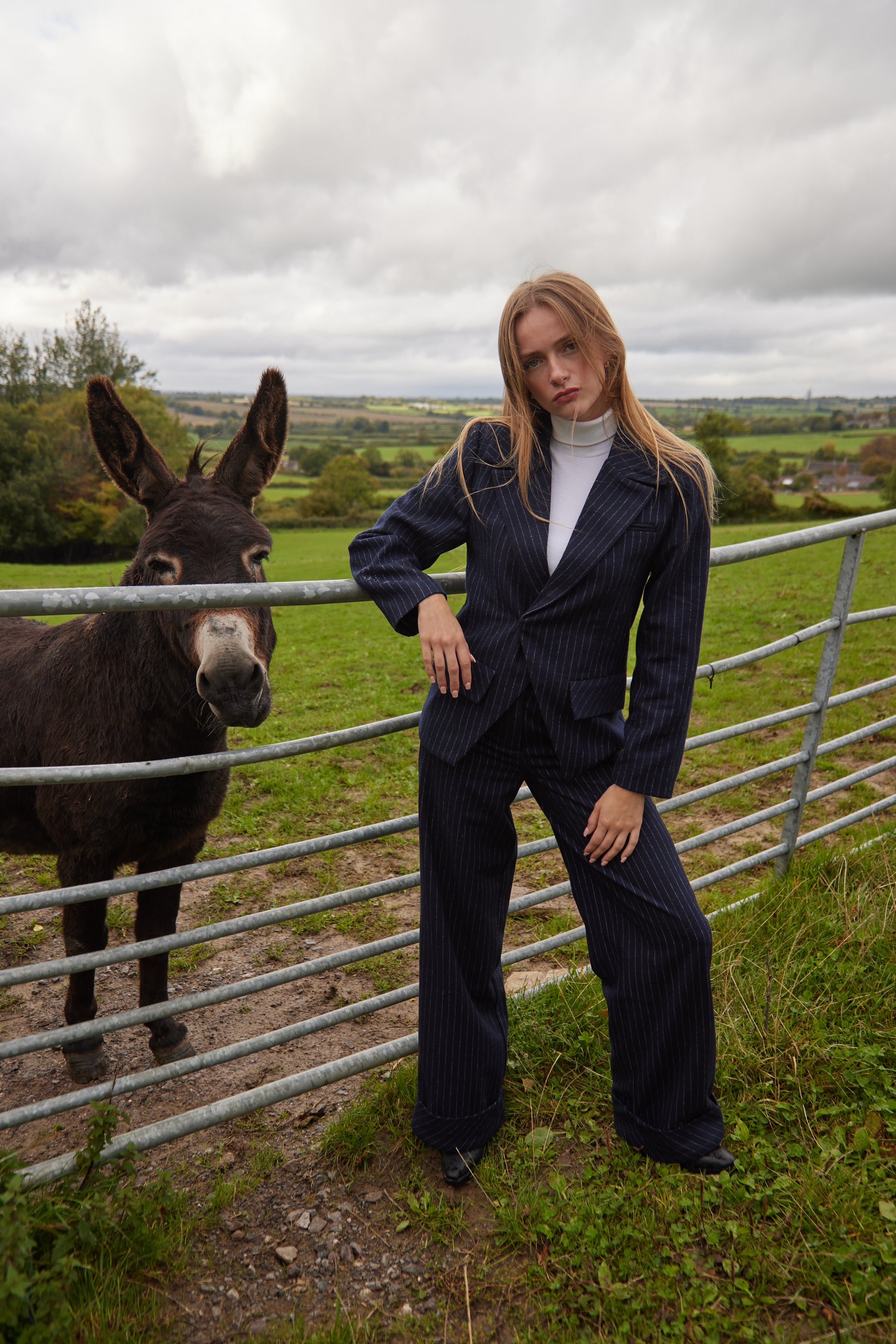 Woman in a suit standing next to a donkey in a field