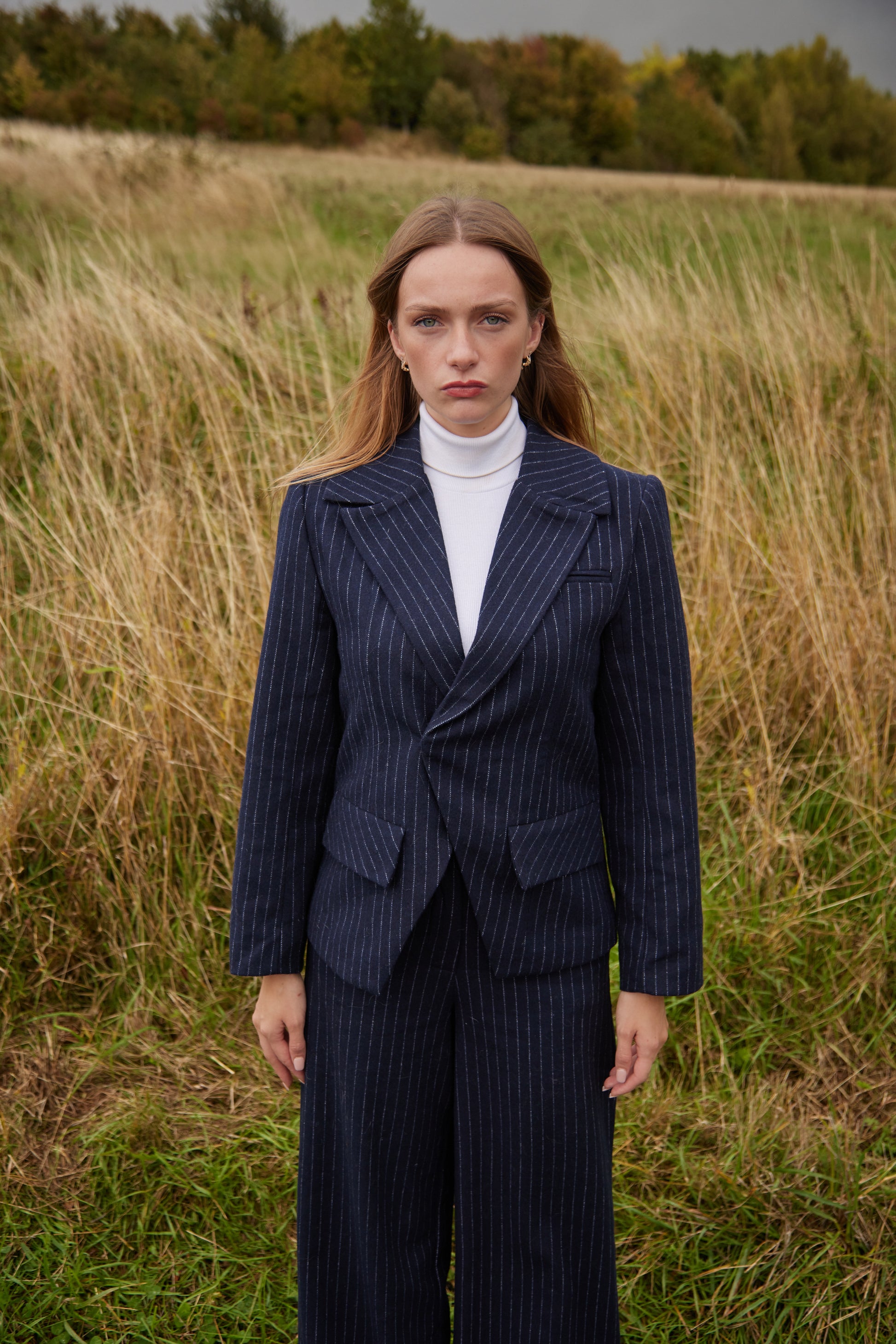 Woman in a navy pinstripe suit standing in a field with trees in the background