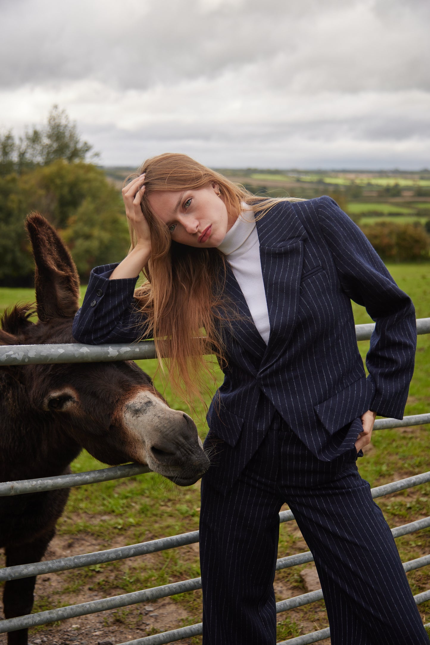 Woman in a pinstripe suit standing next to a donkey in a field