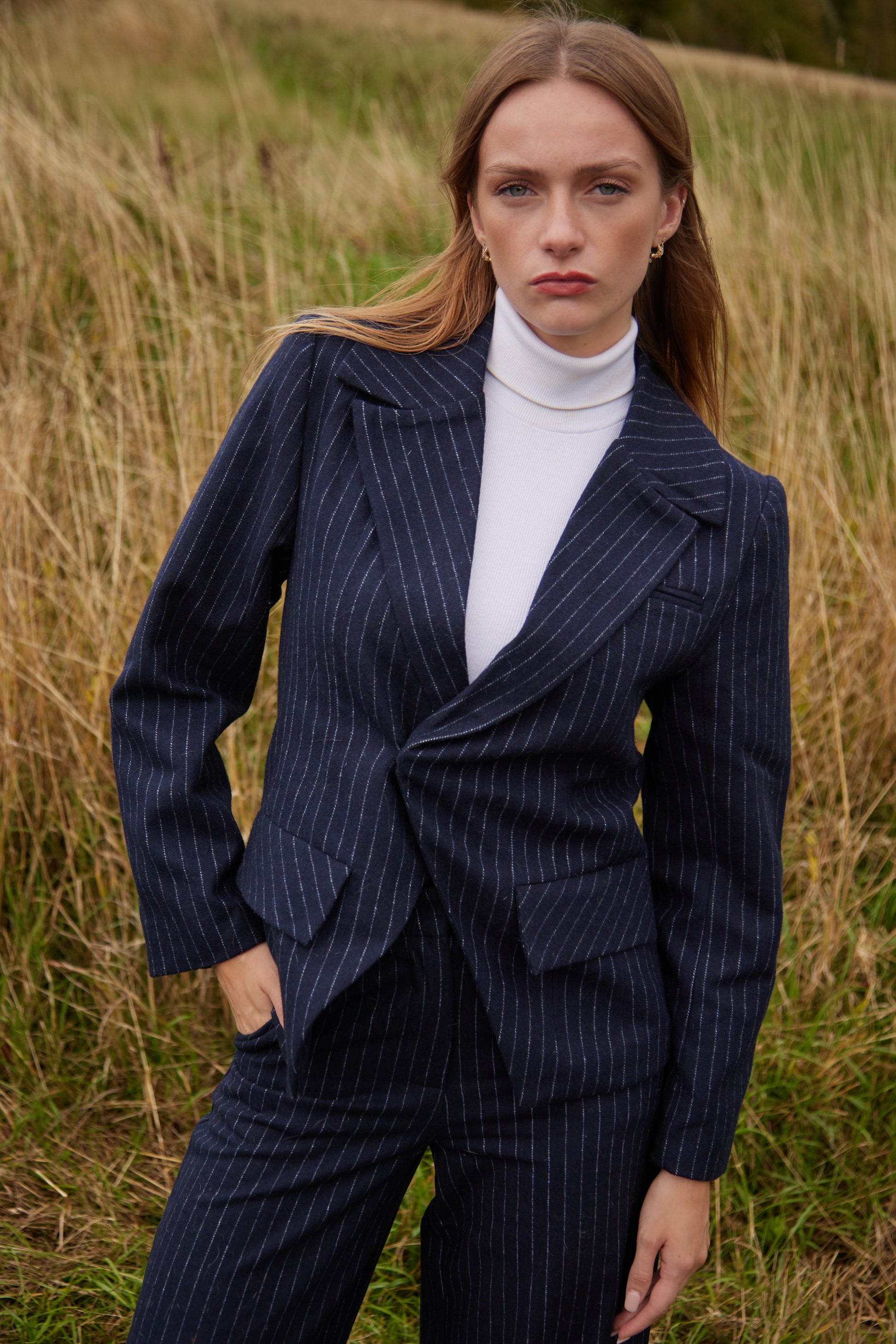 Woman wearing a navy pinstripe suit standing in a grassy field