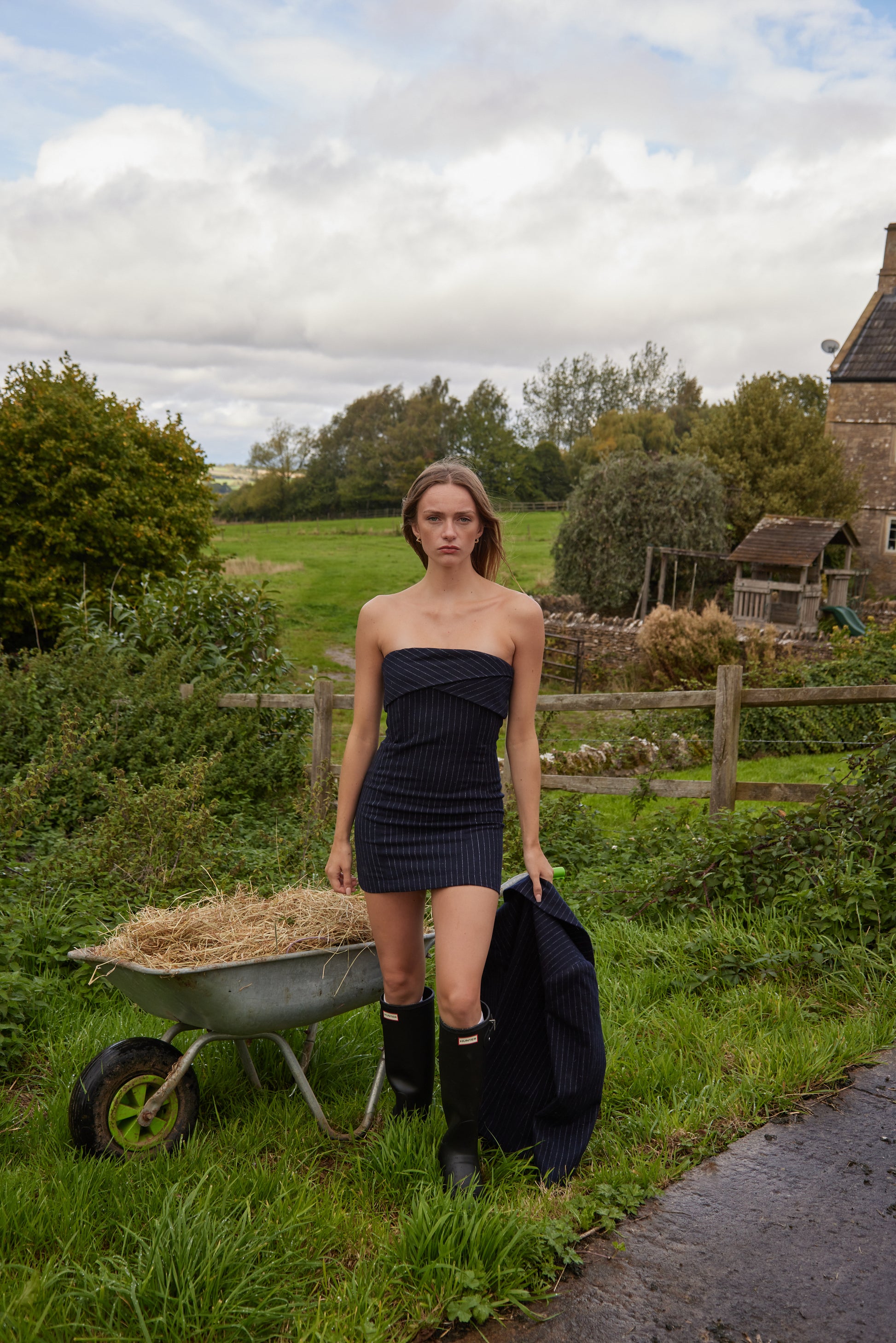 Woman in a strapless dress standing next to a wheelbarrow in a rural setting